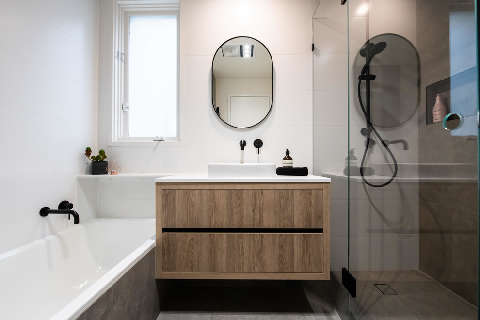Corner shower - mid-sized contemporary master white tile and ceramic tile porcelain tile and brown floor corner shower idea in Melbourne with medium tone wood cabinets, white walls, a vessel sink, quartz countertops, a hinged shower door, white countertops and flat-panel cabinets