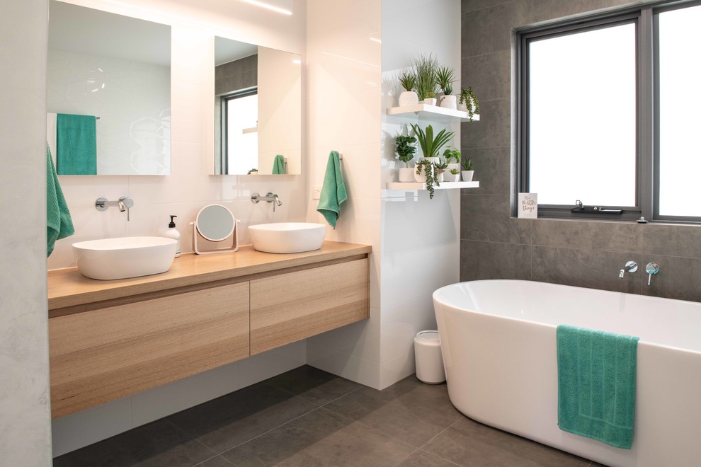 Exemple d'une salle de bain principale tendance en bois clair avec un placard à porte plane, une baignoire indépendante, un carrelage gris, un mur blanc, une vasque, un plan de toilette en bois, un sol gris et un plan de toilette marron.