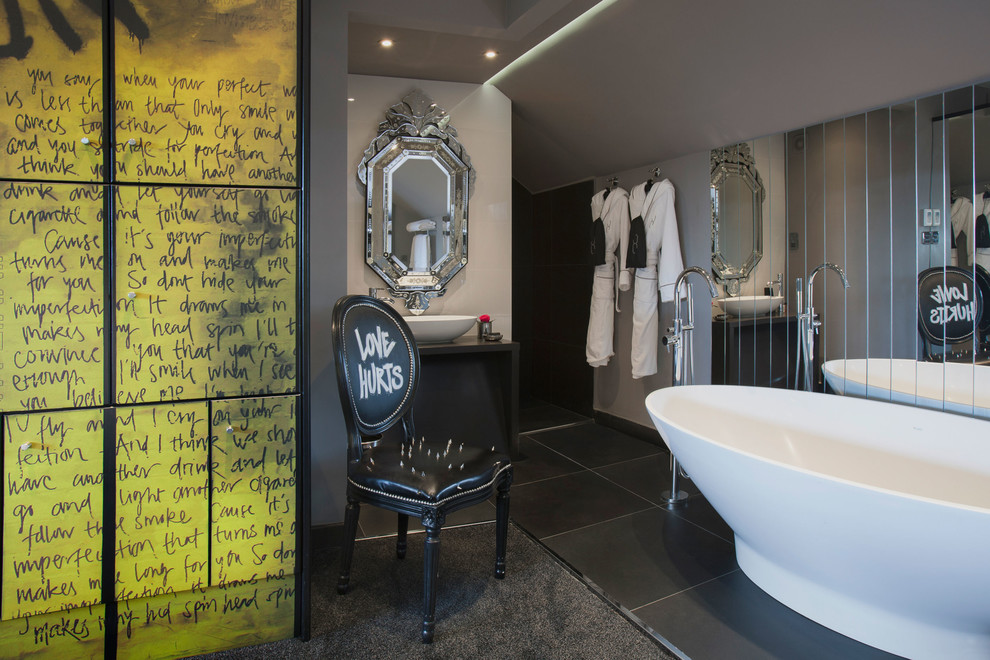Imagen de cuarto de baño contemporáneo con lavabo sobreencimera, puertas de armario negras, bañera exenta y paredes grises