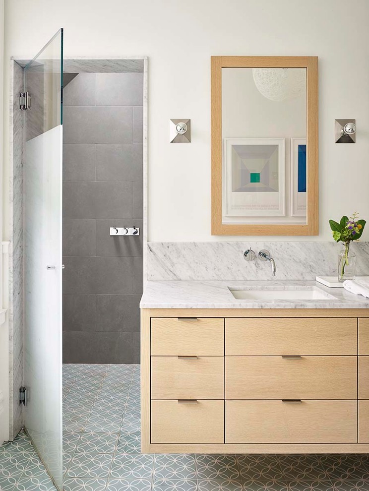 Skandinavisk inredning av ett vit vitt badrum, med släta luckor, skåp i ljust trä, grå kakel, vita väggar, ett undermonterad handfat, marmorbänkskiva, flerfärgat golv och dusch med gångjärnsdörr