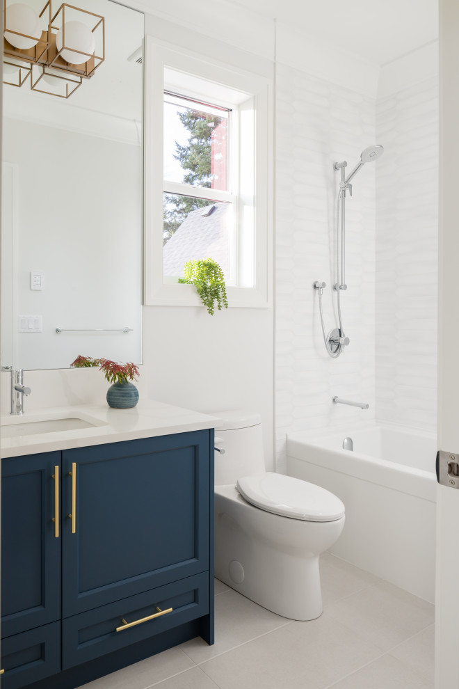 На фото: ванная комната среднего размера в стиле неоклассика (современная классика) с фасадами в стиле шейкер, синими фасадами, душем над ванной, белой плиткой, керамогранитной плиткой, белыми стенами, полом из керамогранита, врезной раковиной, столешницей из искусственного кварца, серым полом, белой столешницей, ванной в нише, унитазом-моноблоком, душевой кабиной, открытым душем, тумбой под одну раковину и встроенной тумбой с