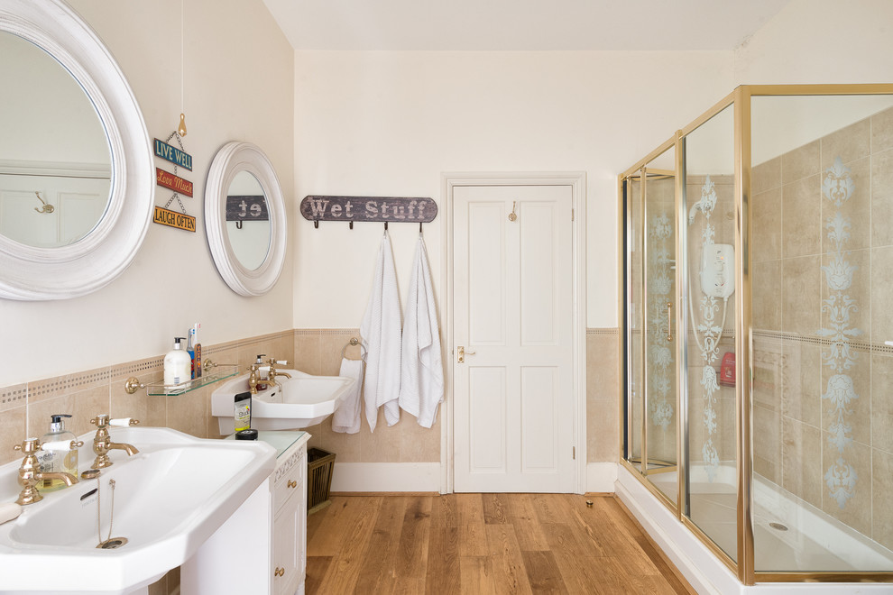 Photo of a medium sized farmhouse bathroom in Devon with a wall-mounted sink, white cabinets, a corner shower, beige tiles, ceramic tiles, beige walls, medium hardwood flooring and recessed-panel cabinets.