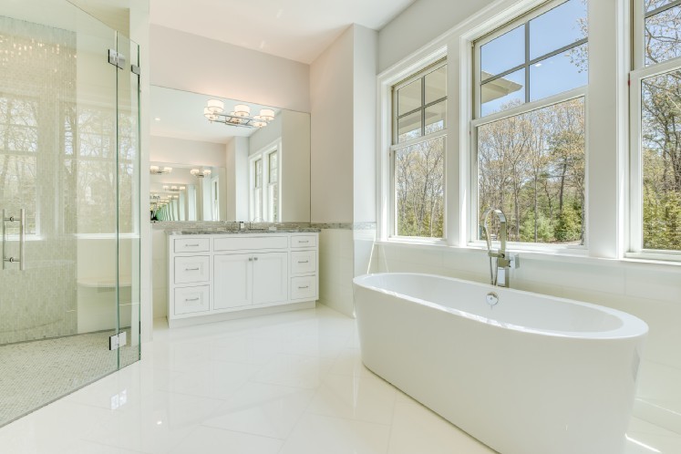Photo of an expansive beach style ensuite bathroom in New York with recessed-panel cabinets, white cabinets, a freestanding bath, a corner shower, a wall mounted toilet, white tiles, white walls, a submerged sink and quartz worktops.