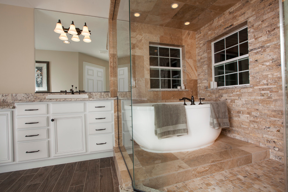 Bild på ett rustikt en-suite badrum, med ett undermonterad handfat, luckor med infälld panel, vita skåp, granitbänkskiva, ett fristående badkar, en toalettstol med separat cisternkåpa, beige kakel, stenkakel, beige väggar och klinkergolv i porslin
