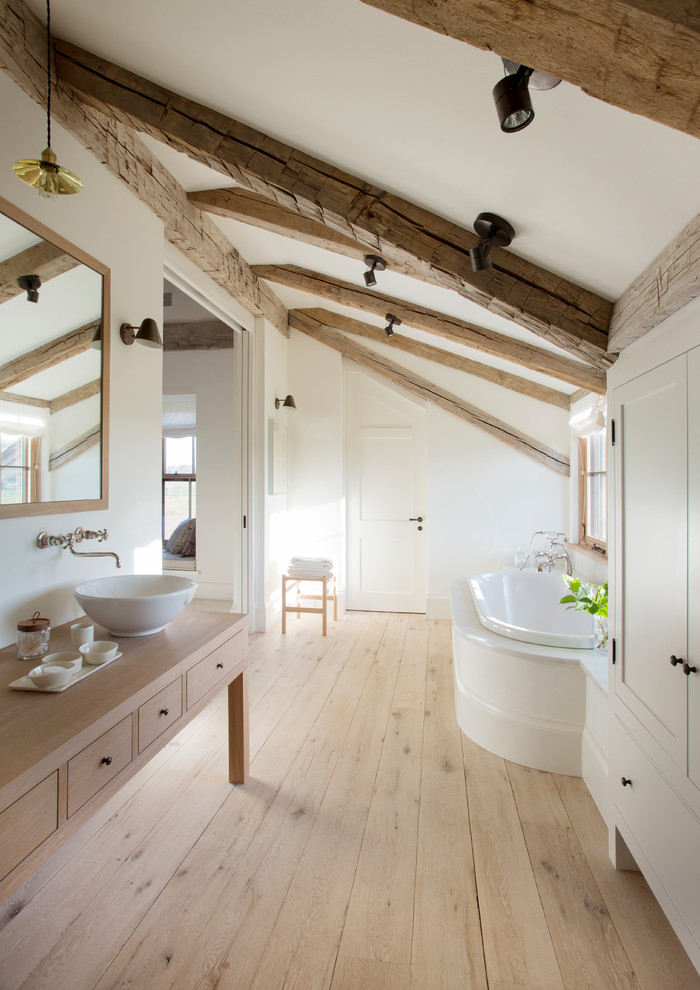 Expansive farmhouse ensuite bathroom in Boston with flat-panel cabinets, light wood cabinets, wooden worktops, a built-in bath, stone slabs, beige worktops, white walls, light hardwood flooring, a vessel sink and brown floors.