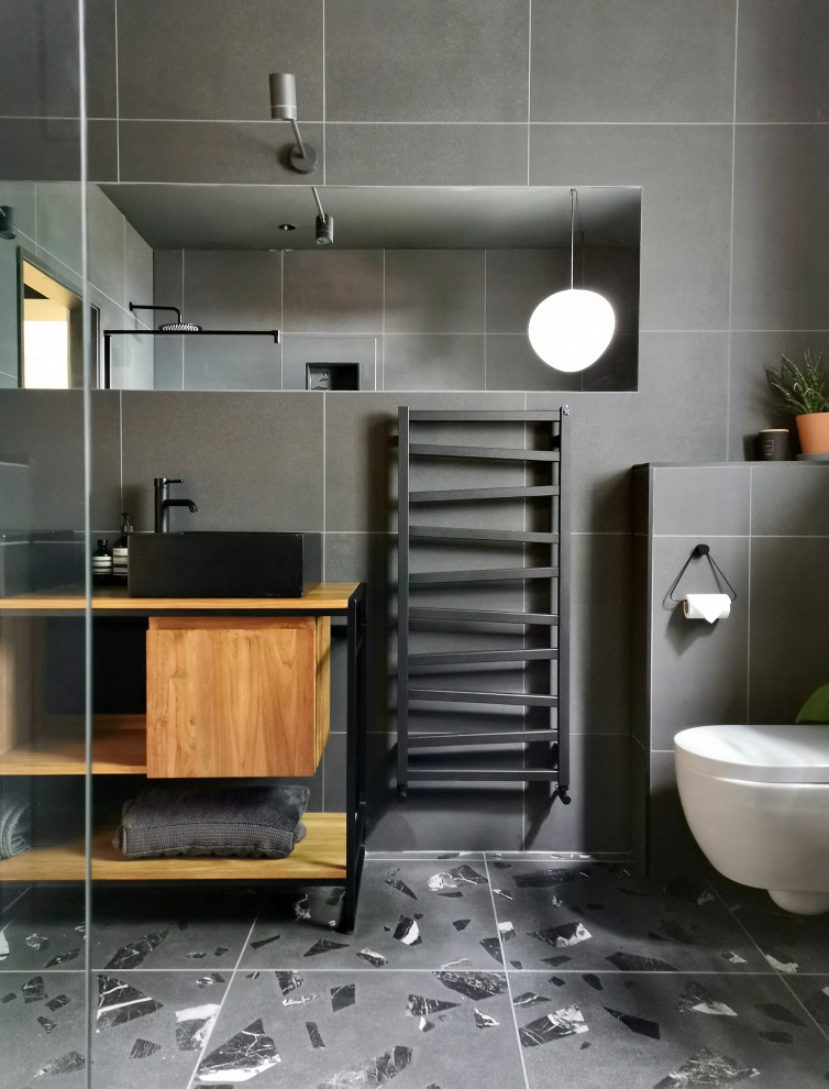 Nordisk inredning av ett mellanstort en-suite badrum, med skåp i mellenmörkt trä, ett fristående badkar, en öppen dusch, en vägghängd toalettstol, grå kakel, porslinskakel, grå väggar, klinkergolv i porslin, ett konsol handfat, träbänkskiva, grått golv och med dusch som är öppen