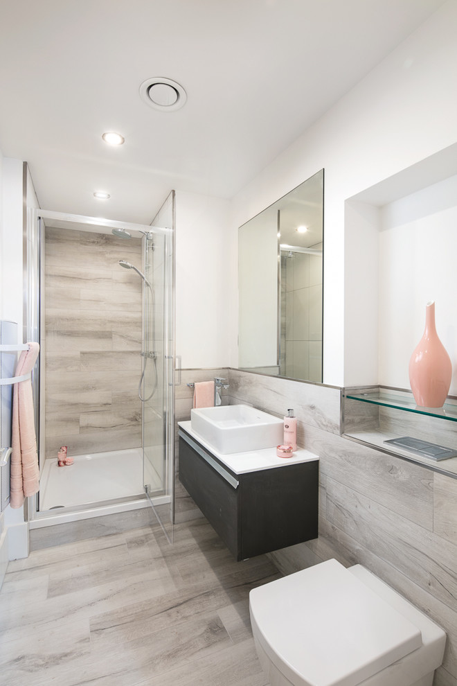 Modern inredning av ett badrum med dusch, med släta luckor, svarta skåp, en dusch i en alkov, en vägghängd toalettstol, grå kakel, ett avlångt handfat, grått golv och dusch med gångjärnsdörr