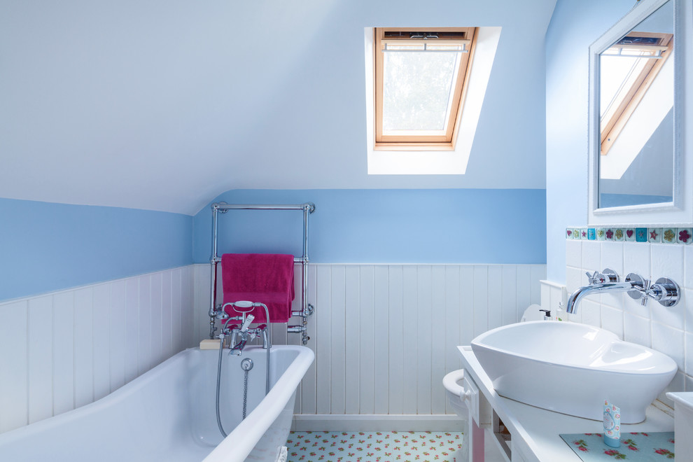 Diseño de cuarto de baño campestre con puertas de armario blancas, bañera exenta, baldosas y/o azulejos blancos, paredes azules, lavabo sobreencimera y suelo multicolor
