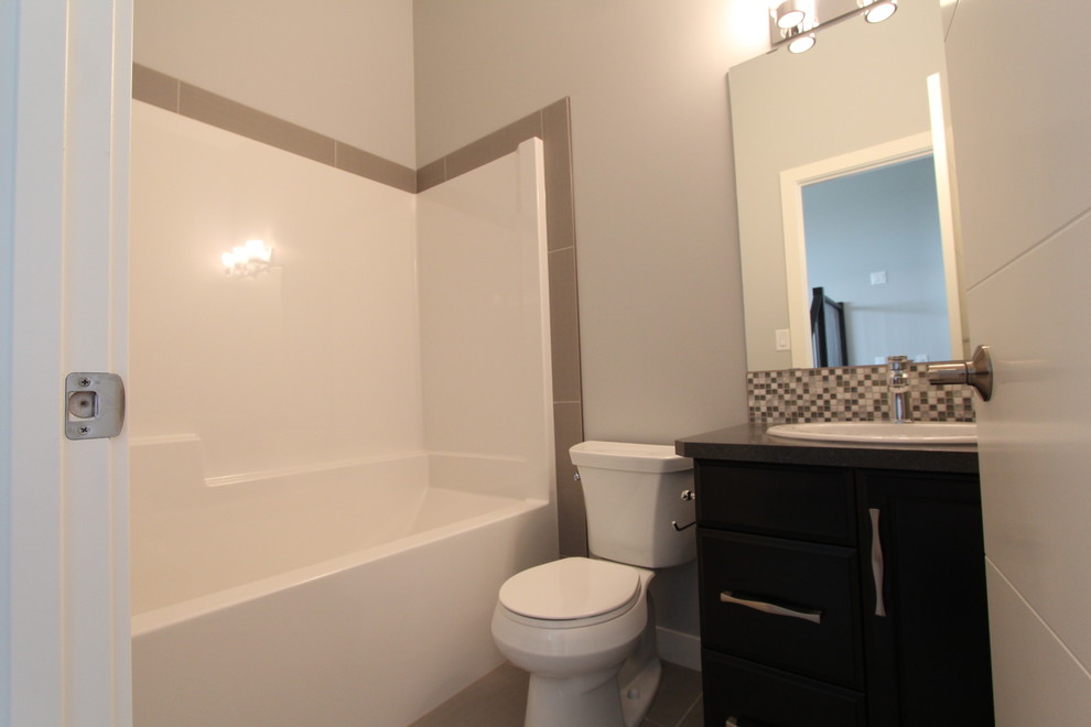 Small arts and crafts gray tile and mosaic tile ceramic tile bathroom photo in Calgary with a drop-in sink, flat-panel cabinets, dark wood cabinets, laminate countertops, a one-piece toilet and gray walls