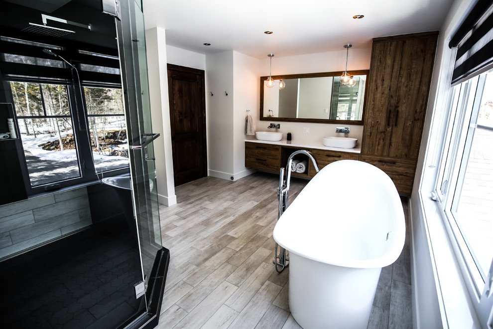 Cette image montre une grande salle de bain principale chalet en bois brun avec un placard à porte plane, une baignoire indépendante, une douche d'angle, un carrelage noir et blanc, des carreaux de porcelaine, un mur gris, un sol en carrelage de porcelaine, une vasque et un plan de toilette en stratifié.