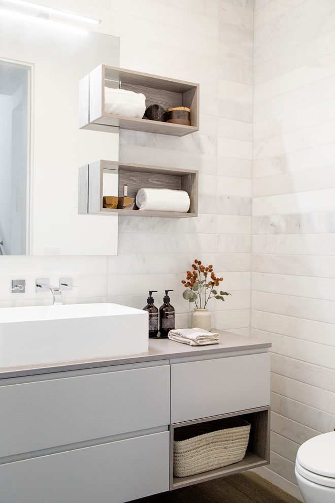 Modernes Badezimmer mit flächenbündigen Schrankfronten, grauen Schränken, Wandtoilette, weißen Fliesen, Marmorfliesen, weißer Wandfarbe, dunklem Holzboden, Aufsatzwaschbecken, braunem Boden und grauer Waschtischplatte in Los Angeles