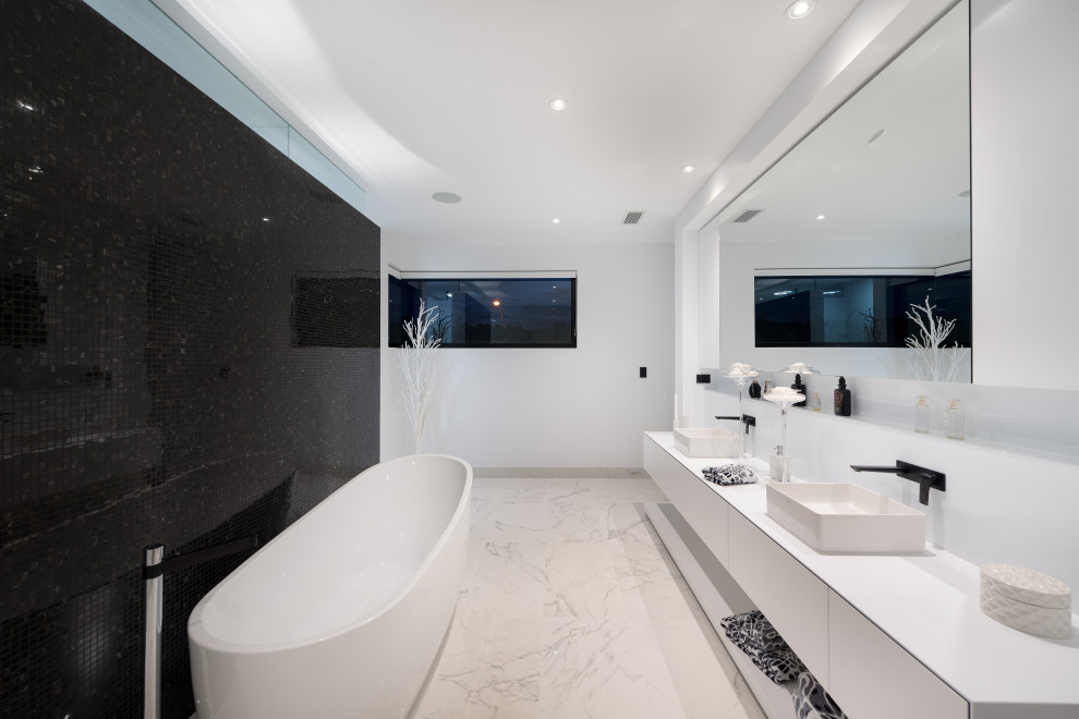 На фото: большая главная ванная комната в современном стиле с плоскими фасадами, белыми фасадами, отдельно стоящей ванной, черной плиткой, белыми стенами, настольной раковиной, бежевым полом, белой столешницей и подвесной тумбой