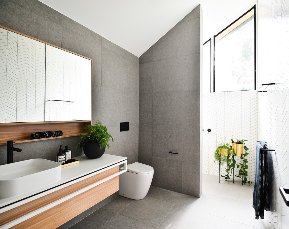 Inredning av ett modernt vit vitt badrum, med släta luckor, skåp i mellenmörkt trä, en kantlös dusch, grå kakel, ett fristående handfat, grått golv och med dusch som är öppen