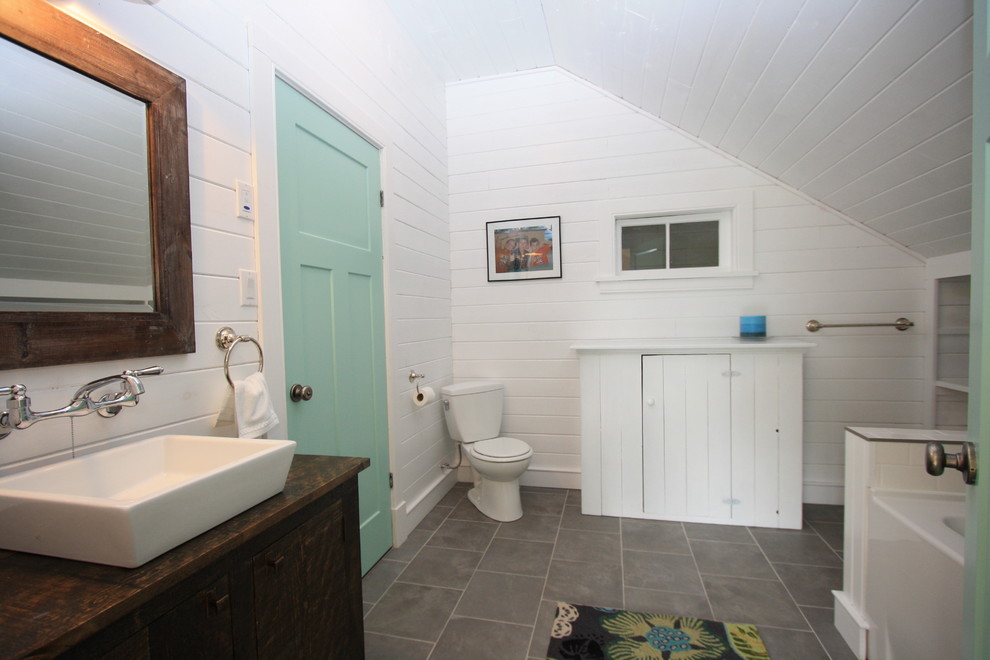Cette image montre une salle de bain chalet en bois foncé avec une vasque, un placard à porte plane, une baignoire en alcôve, WC séparés et un carrelage gris.
