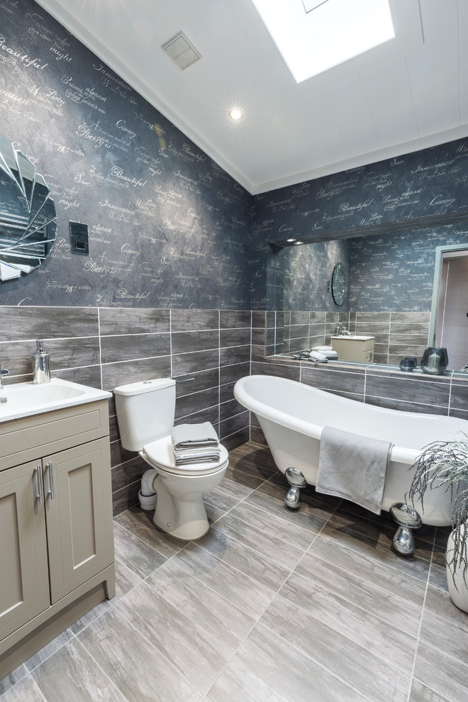 Bild på ett mellanstort maritimt badrum, med luckor med infälld panel, beige skåp, ett badkar med tassar, en toalettstol med hel cisternkåpa, grå kakel, grå väggar, ett undermonterad handfat och grått golv