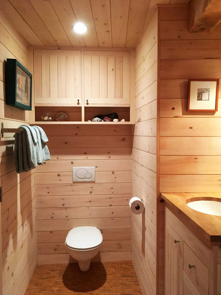 Modern inredning av ett litet badrum, med skåp i ljust trä, ett hörnbadkar, en dusch/badkar-kombination, en vägghängd toalettstol, ett undermonterad handfat och träbänkskiva