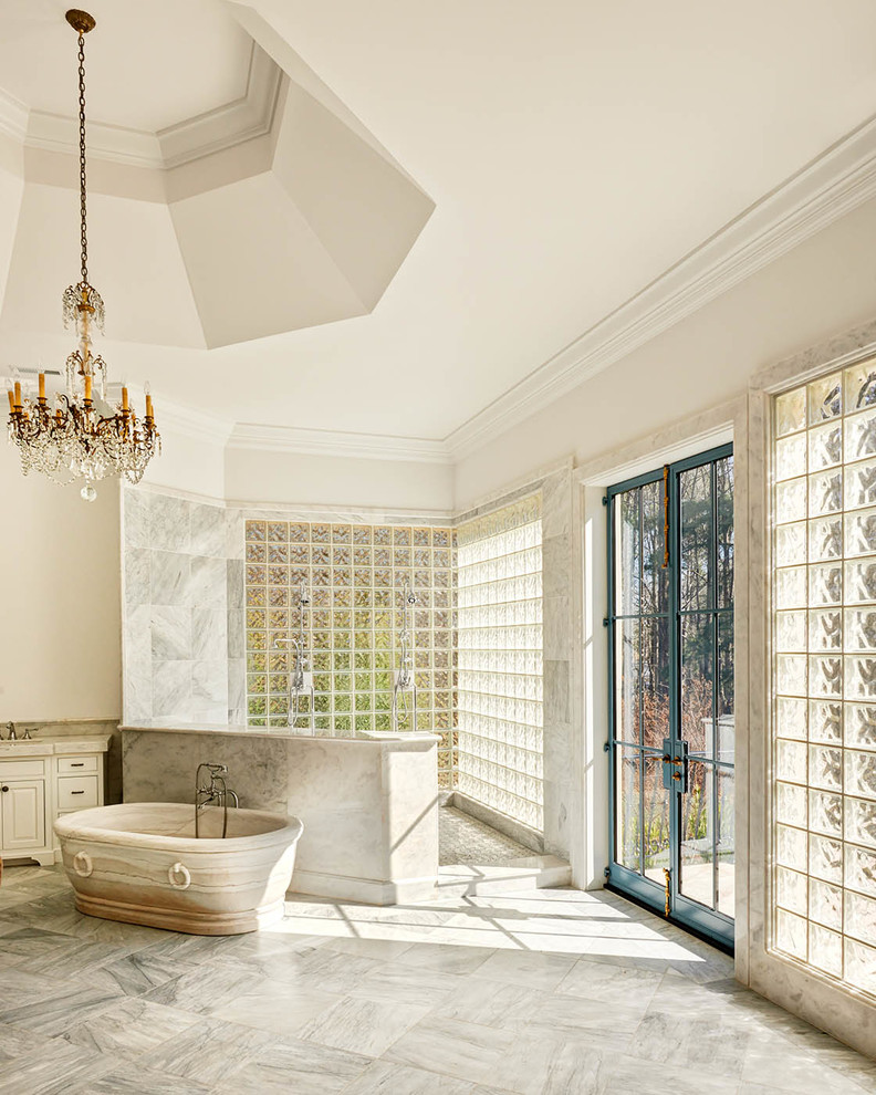 Inredning av ett klassiskt mycket stort en-suite badrum, med ett konsol handfat, vita skåp, marmorbänkskiva, ett fristående badkar, en öppen dusch, beige kakel, vita väggar och marmorgolv