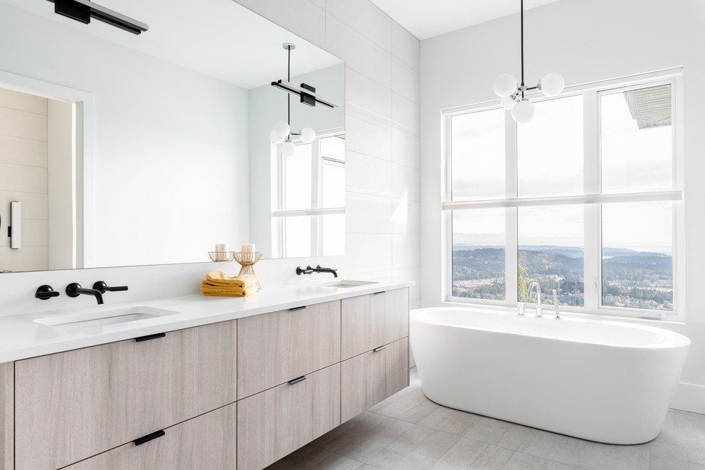 Modern inredning av ett vit vitt badrum, med släta luckor, grå skåp, ett fristående badkar, vit kakel, vita väggar, ett undermonterad handfat och grått golv