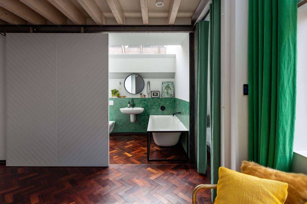 Inspiration for a medium sized contemporary ensuite bathroom in London with flat-panel cabinets, white cabinets, a freestanding bath, a walk-in shower, a wall mounted toilet, green tiles, ceramic tiles, green walls, dark hardwood flooring, a wall-mounted sink, tiled worktops, brown floors, an open shower and green worktops.