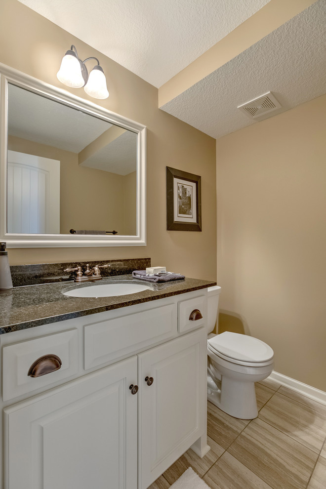 Cette photo montre une salle de bain craftsman de taille moyenne avec un placard avec porte à panneau surélevé, des portes de placard blanches, un plan de toilette en granite, un carrelage beige, un mur beige, un sol en carrelage de céramique, un sol beige et un lavabo encastré.