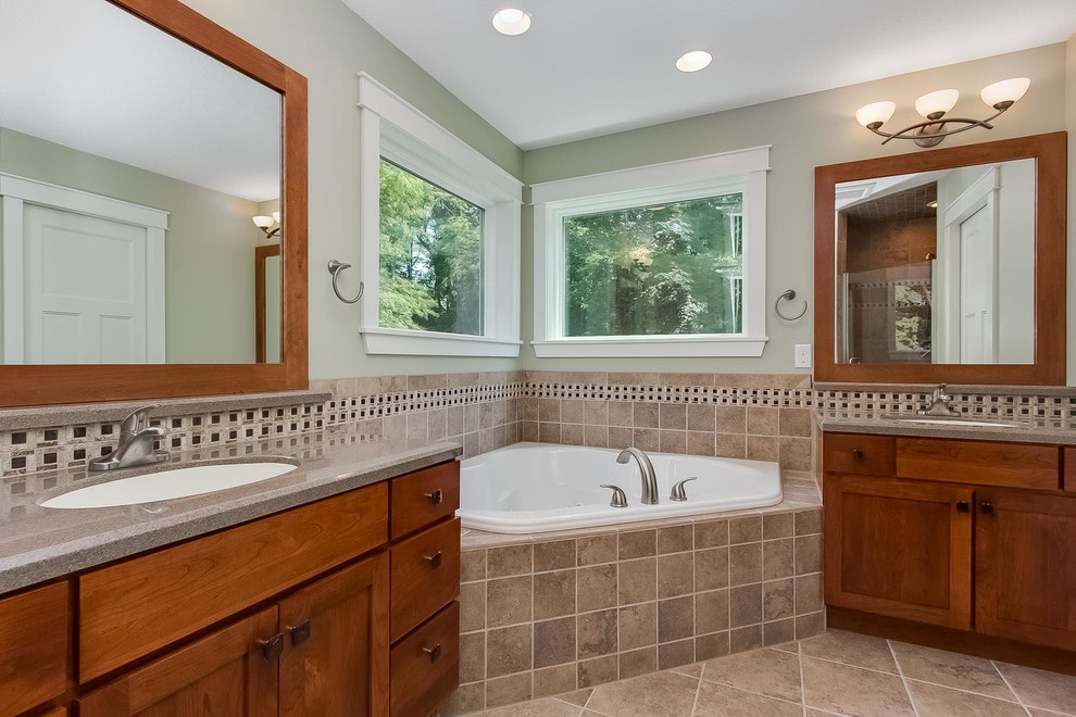 Photo of a medium sized country ensuite bathroom in Minneapolis with an integrated sink, shaker cabinets, medium wood cabinets, solid surface worktops, a corner bath, a corner shower, a one-piece toilet, beige tiles, ceramic tiles, green walls and ceramic flooring.