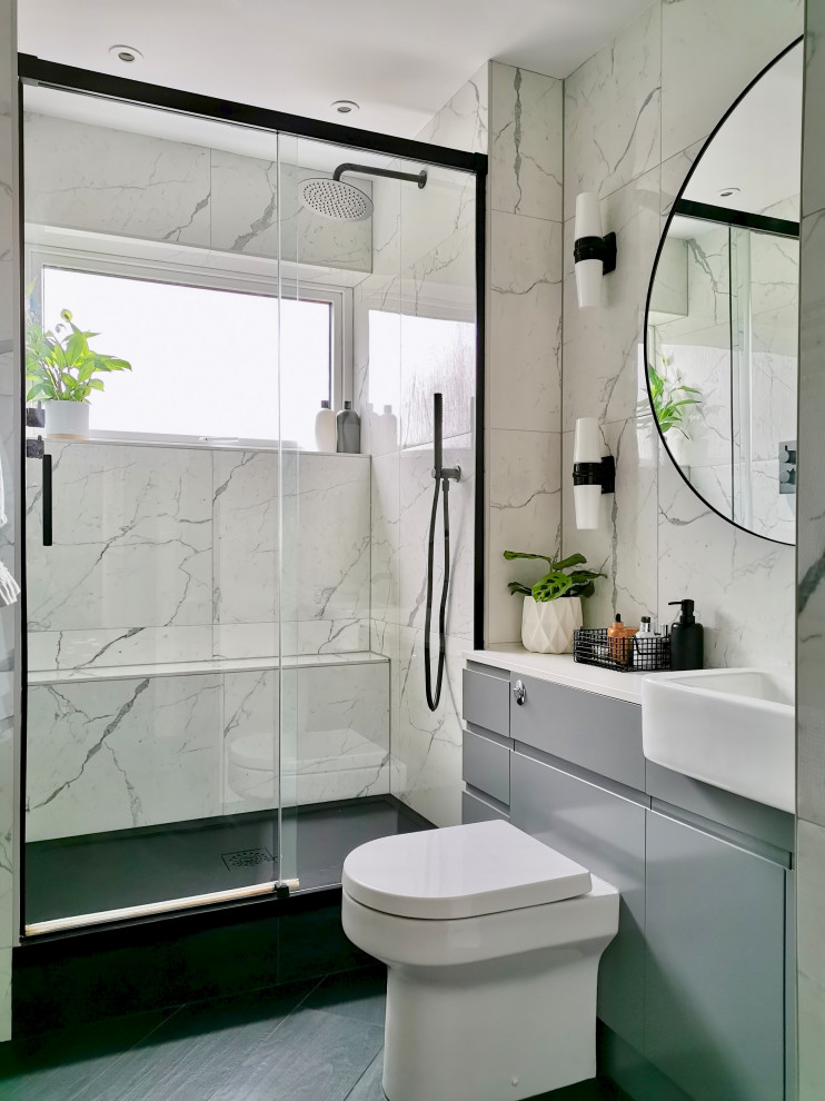 На фото: маленькая ванная комната в современном стиле с плоскими фасадами, серыми фасадами, душем без бортиков, унитазом-моноблоком, белой плиткой, керамической плиткой, белыми стенами, полом из керамогранита, душевой кабиной, монолитной раковиной, черным полом, душем с раздвижными дверями, белой столешницей, тумбой под одну раковину и встроенной тумбой для на участке и в саду