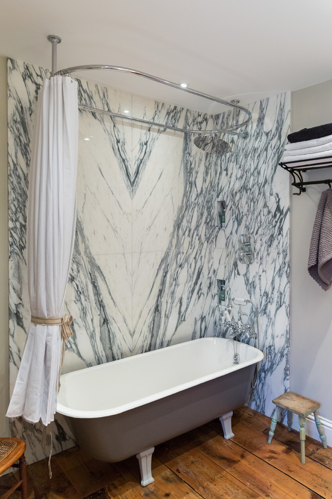 Réalisation d'une salle de bain principale tradition avec du carrelage en marbre, une baignoire sur pieds, un combiné douche/baignoire, un mur gris, un sol en bois brun et un sol orange.