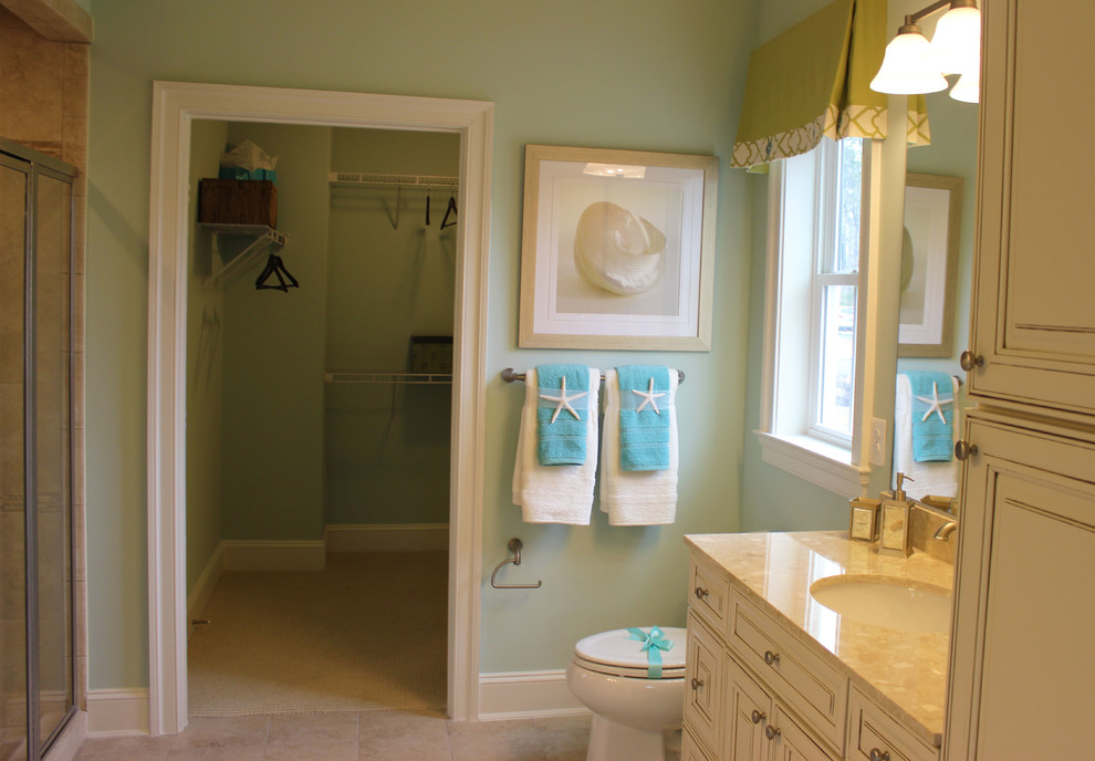 Modelo de cuarto de baño principal costero con puertas de armario blancas, encimera de granito, baldosas y/o azulejos beige y paredes azules