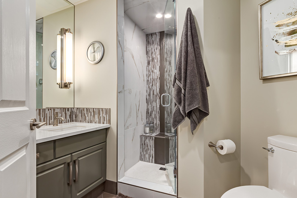 Design ideas for a classic ensuite bathroom in Calgary with a freestanding bath, grey cabinets, an alcove shower, a one-piece toilet, brown tiles, glass sheet walls, beige walls, ceramic flooring, a submerged sink, engineered stone worktops and flat-panel cabinets.