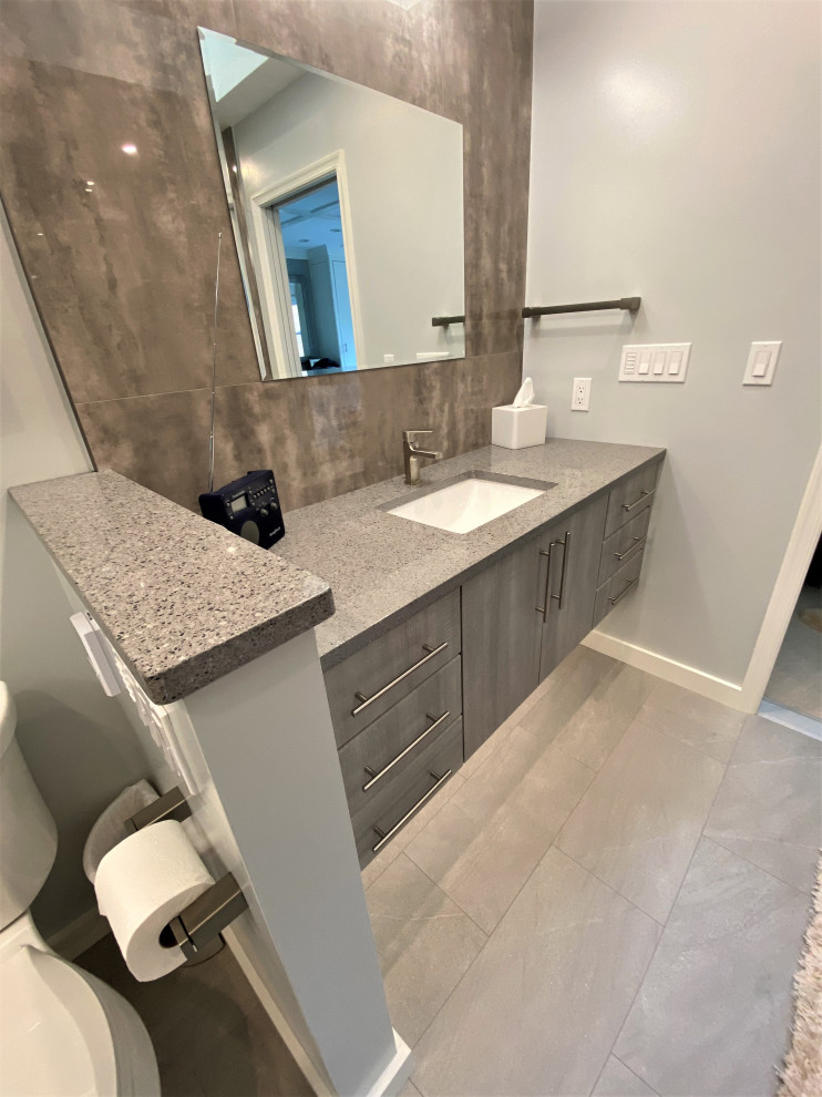 Inspiration for a medium sized contemporary ensuite bathroom in DC Metro with flat-panel cabinets, grey cabinets, an alcove shower, a two-piece toilet, grey tiles, porcelain tiles, grey walls, porcelain flooring, a submerged sink, engineered stone worktops, grey floors, a hinged door, grey worktops, a shower bench, double sinks and a floating vanity unit.