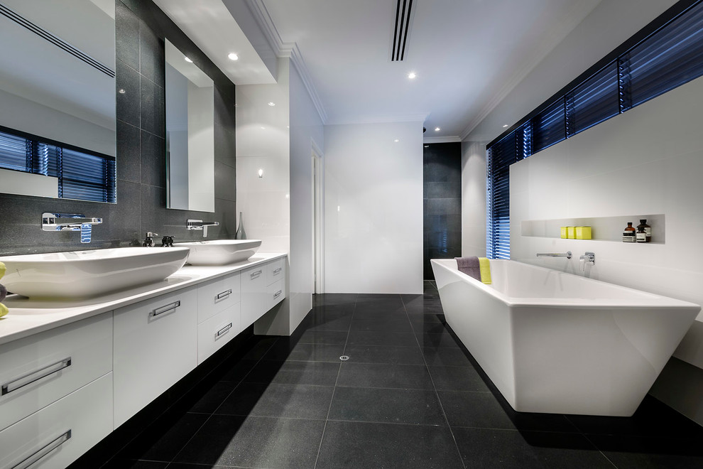 Exemple d'une salle de bain tendance avec une vasque, un placard à porte plane, des portes de placard blanches, une baignoire indépendante, un carrelage gris et un mur blanc.