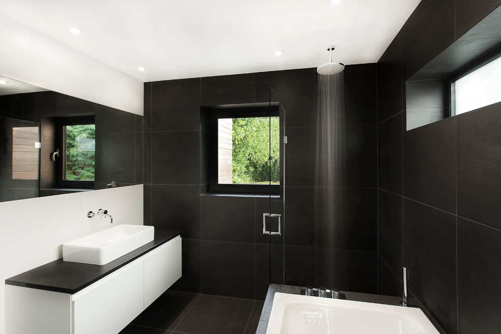 Cette photo montre une salle de bain tendance avec une vasque, un placard à porte plane, des portes de placard blanches, une baignoire posée, un combiné douche/baignoire et un carrelage noir.
