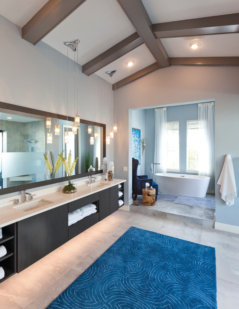 Cette photo montre une salle de bain chic avec un placard à porte plane, des portes de placard noires, une baignoire indépendante, un mur gris, un lavabo encastré, un sol gris et un plan de toilette beige.
