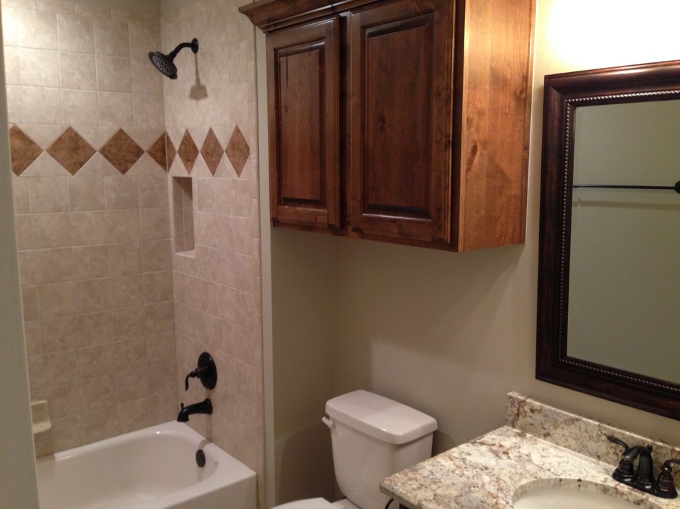 Cette image montre une salle de bain traditionnelle en bois brun de taille moyenne avec un placard avec porte à panneau surélevé, un plan de toilette en granite, un combiné douche/baignoire, un mur beige, un sol en bois brun, une baignoire encastrée, WC séparés, un carrelage beige, des carreaux de céramique et un lavabo encastré.