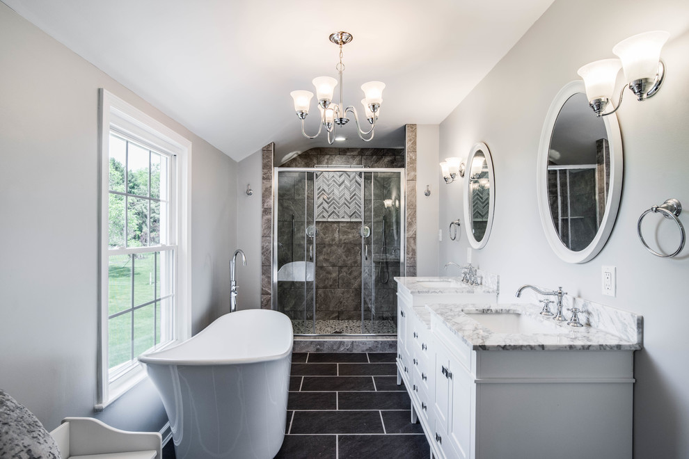 Idée de décoration pour une douche en alcôve principale tradition avec des portes de placard blanches, une baignoire indépendante, un carrelage gris, un mur gris, un lavabo encastré, un sol noir et un placard à porte shaker.