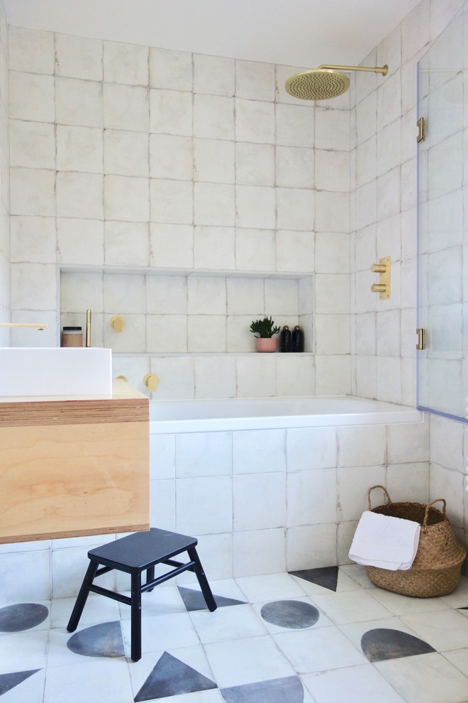 Photo of a scandinavian family bathroom in Other with light wood cabinets, a built-in bath, a shower/bath combination, a one-piece toilet, black and white tiles, porcelain tiles, white walls, porcelain flooring, a console sink, wooden worktops and multi-coloured floors.