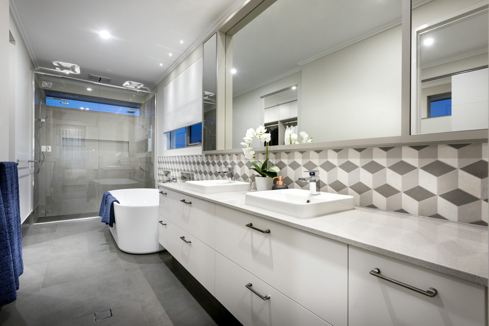 Idée de décoration pour une douche en alcôve principale design avec un placard à porte plane, des portes de placard blanches, une baignoire indépendante, un carrelage gris, un mur multicolore et un lavabo posé.