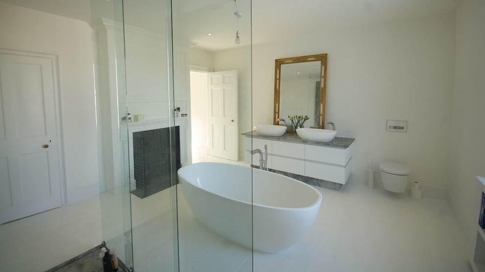 На фото: ванная комната среднего размера в современном стиле с плоскими фасадами, белыми фасадами, отдельно стоящей ванной, открытым душем, инсталляцией, белыми стенами, деревянным полом, настольной раковиной и мраморной столешницей