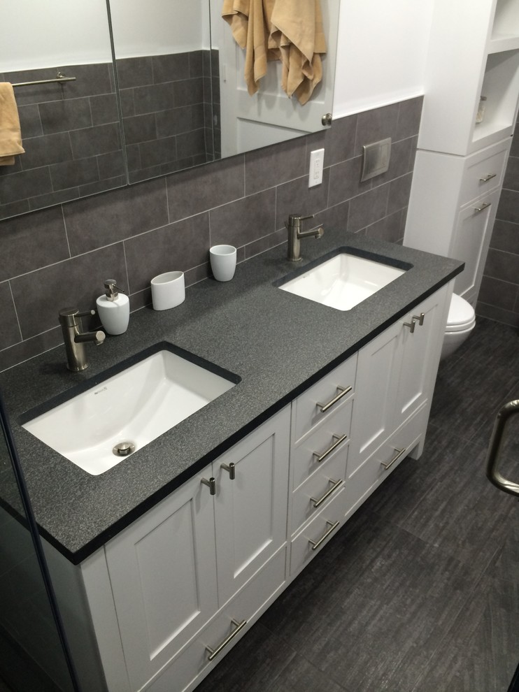 Photo of a modern ensuite bathroom in New York with a submerged sink, shaker cabinets, white cabinets, quartz worktops, a double shower, a wall mounted toilet, grey tiles, ceramic tiles, white walls and ceramic flooring.