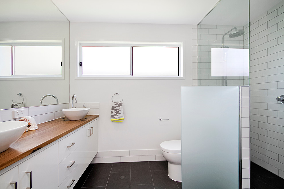 Foto de cuarto de baño actual con encimera de madera, ducha abierta, sanitario de una pieza, baldosas y/o azulejos grises, paredes blancas, suelo de baldosas de cerámica y aseo y ducha
