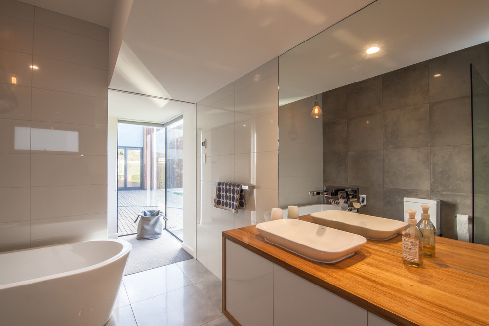 Design ideas for a medium sized contemporary ensuite bathroom in Hobart with flat-panel cabinets, white cabinets, a freestanding bath, a walk-in shower, a one-piece toilet, white tiles, ceramic tiles, white walls, ceramic flooring, a vessel sink and wooden worktops.