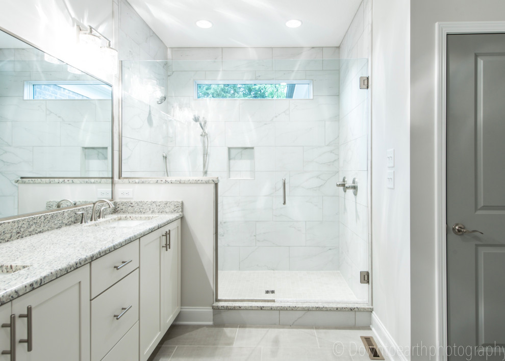 Cette photo montre une salle de bain craftsman avec un placard à porte shaker, des portes de placard blanches, un carrelage blanc, des carreaux de céramique, un mur gris, un sol en carrelage de céramique, un lavabo encastré, un plan de toilette en granite, un sol gris, une cabine de douche à porte battante, un plan de toilette blanc, une niche, meuble double vasque et meuble-lavabo encastré.