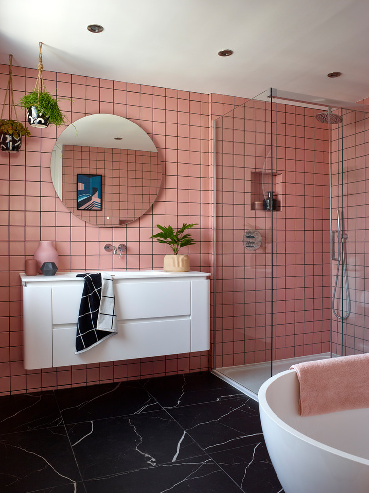 Modernes Badezimmer mit flächenbündigen Schrankfronten, weißen Schränken, freistehender Badewanne, Eckdusche, rosa Fliesen, rosa Wandfarbe, integriertem Waschbecken, schwarzem Boden, Schiebetür-Duschabtrennung und weißer Waschtischplatte in London