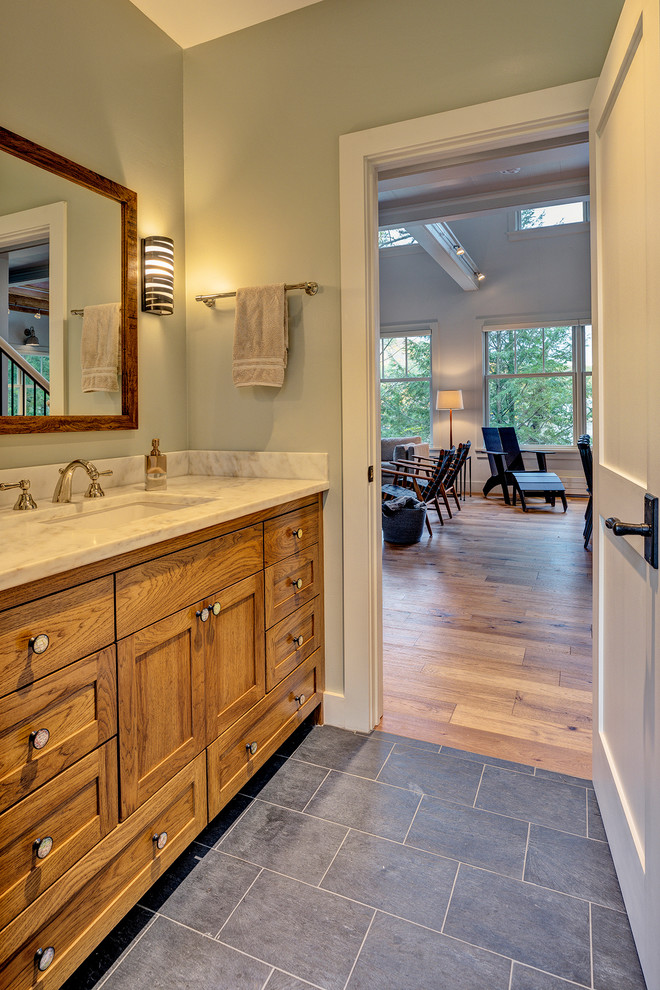 Example of a beach style slate floor and black floor bathroom design in Burlington with shaker cabinets, medium tone wood cabinets, a one-piece toilet, an undermount sink, marble countertops, a hinged shower door and white countertops