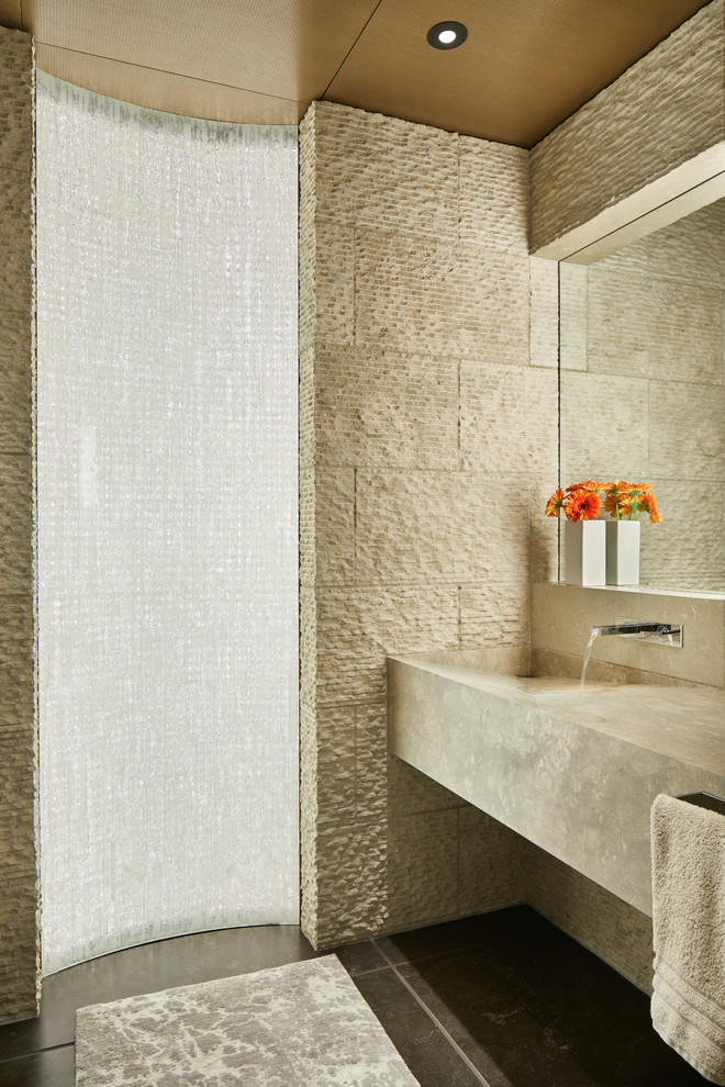 Cette image montre une salle de bain design avec un carrelage beige, un lavabo intégré, un sol noir et un plan de toilette beige.