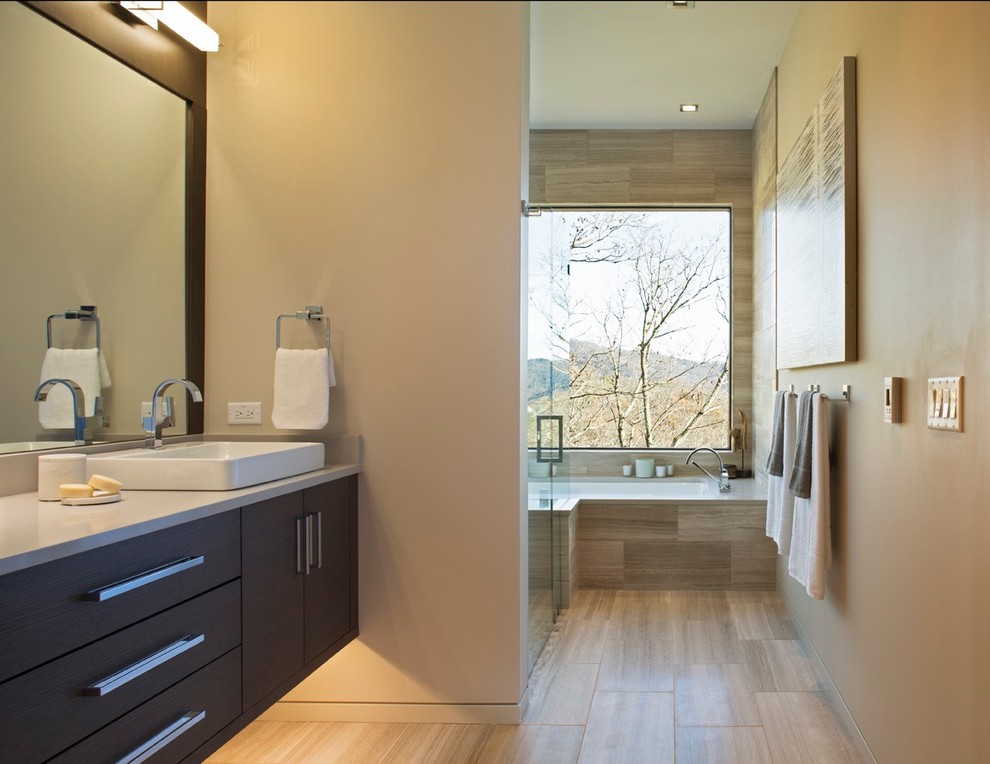Idée de décoration pour une grande salle de bain principale design en bois foncé avec un placard à porte plane, une baignoire posée, un carrelage beige, un carrelage de pierre, une vasque et un plan de toilette en quartz modifié.