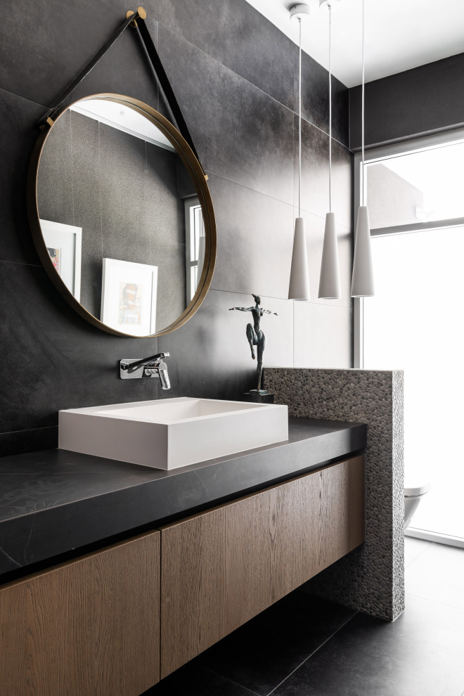 Inspiration pour une salle de bain design en bois brun avec un placard à porte plane, un carrelage noir, une vasque, un sol noir, un plan de toilette noir, meuble simple vasque et meuble-lavabo suspendu.