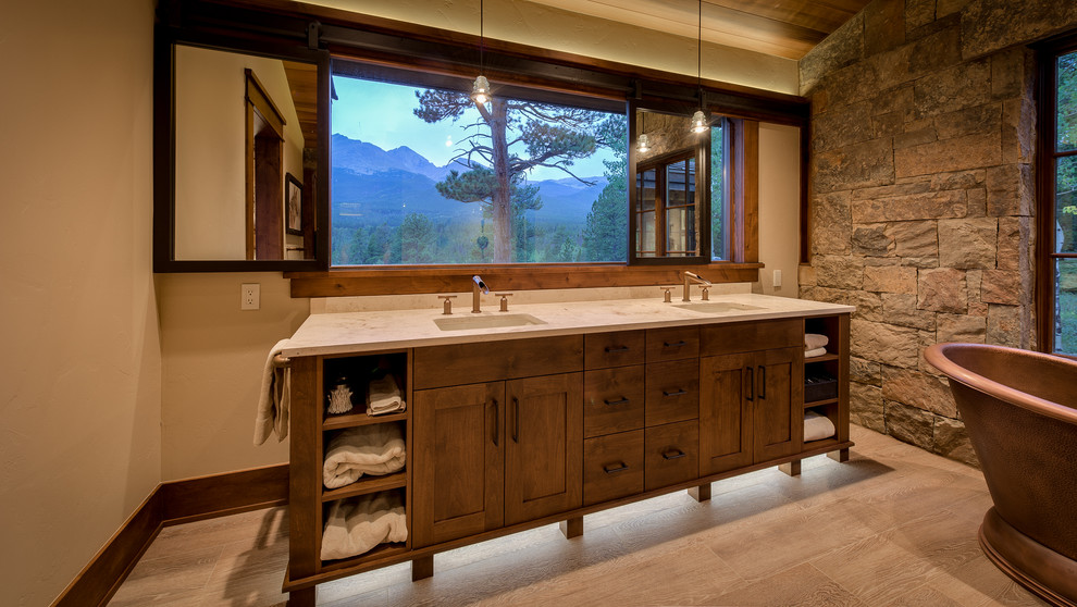 Inspiration for a medium sized rustic ensuite bathroom in Denver with medium wood cabinets, a freestanding bath, a double shower, stone slabs, beige walls, light hardwood flooring, an integrated sink, beige floors, a hinged door and shaker cabinets.