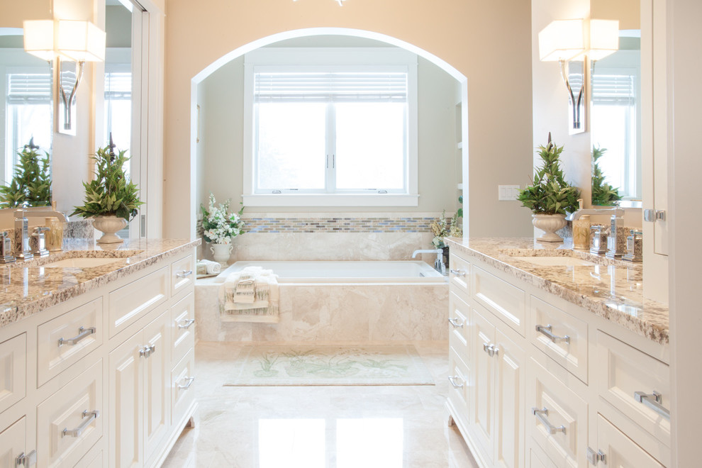 Example of a large classic master beige tile travertine floor drop-in bathtub design in Milwaukee with a drop-in sink, raised-panel cabinets, light wood cabinets, marble countertops and beige walls