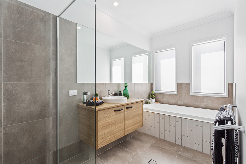 Inredning av ett modernt badrum, med släta luckor, skåp i ljust trä, ett platsbyggt badkar, en kantlös dusch, vita väggar, ett fristående handfat, träbänkskiva, brunt golv och med dusch som är öppen